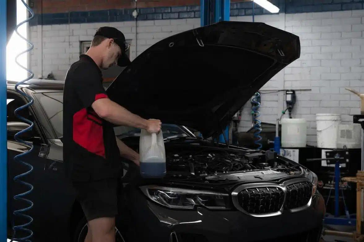 Pace Auto Werks mechanic pouring liquid from a jug into a car bonnet