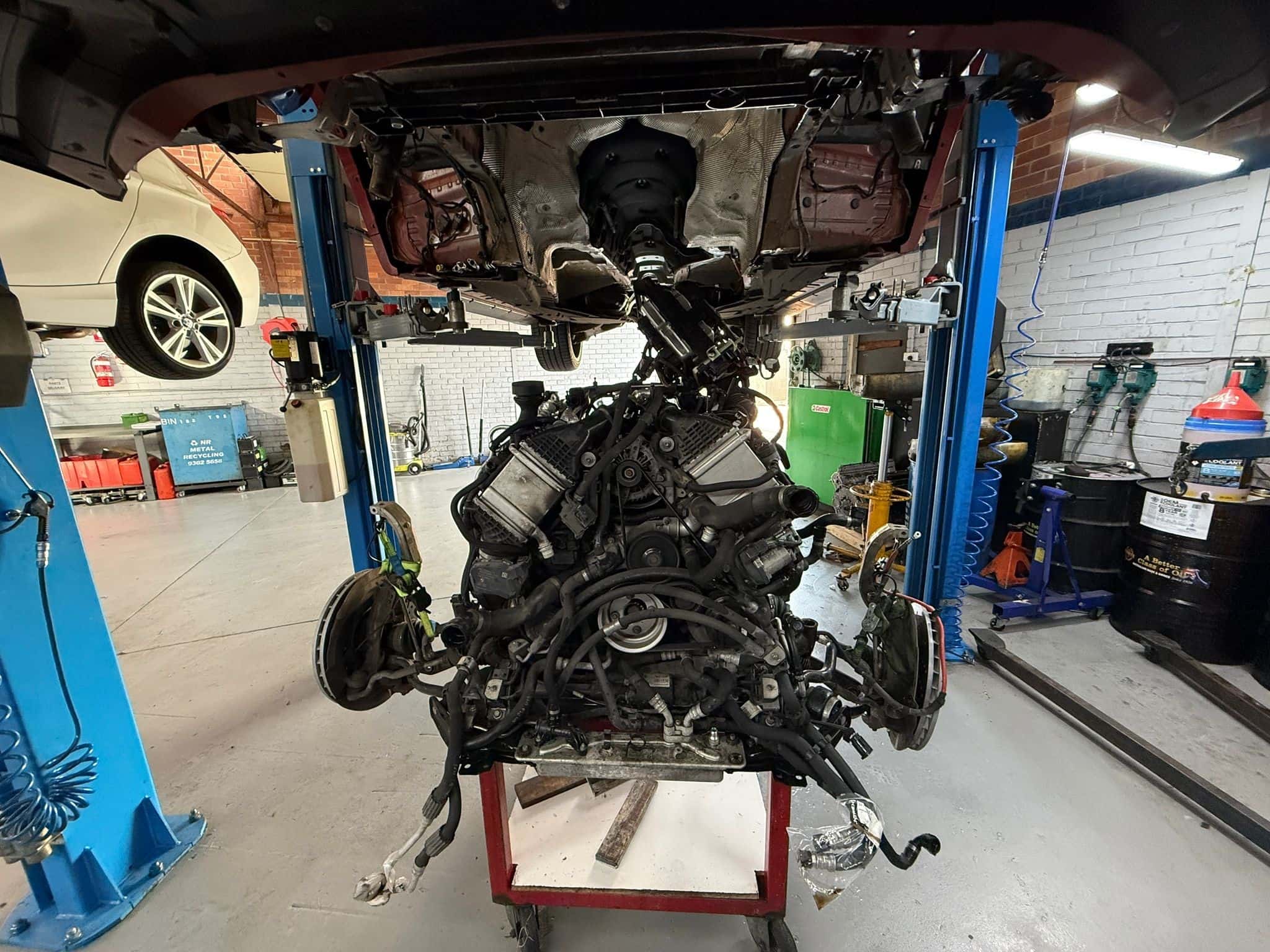 View underneath a BMW X5M on a hoist with the S63 engine removed for valve stem seal replacement
