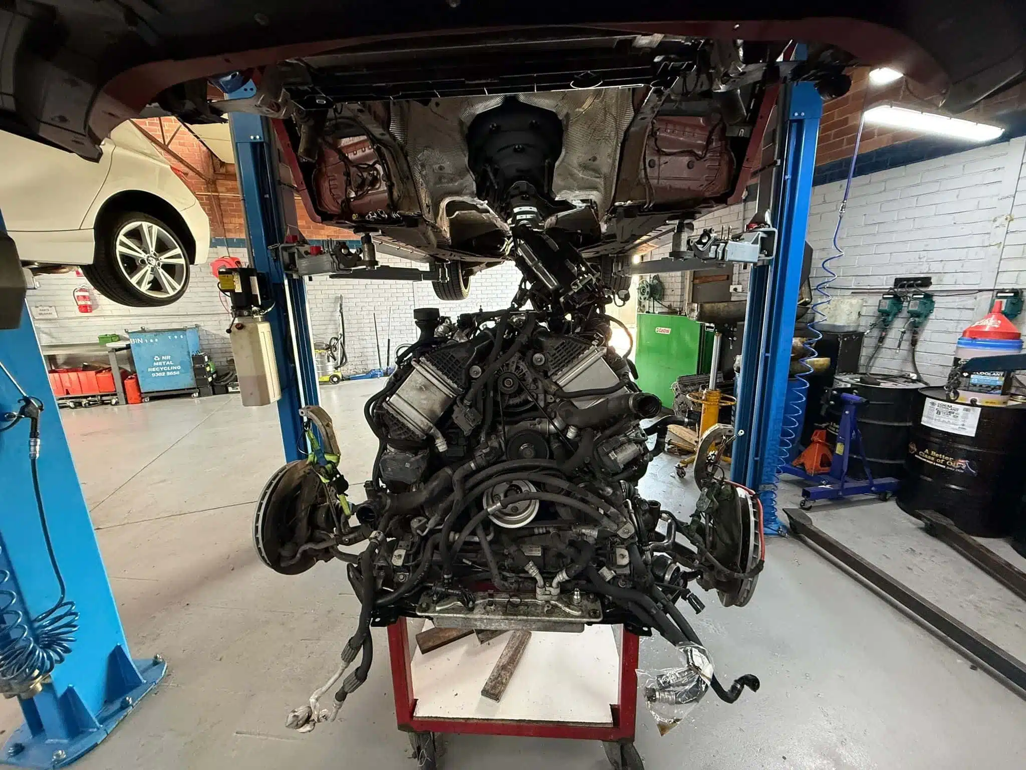 View underneath a BMW X5M on a hoist with the S63 engine removed for valve stem seal replacement