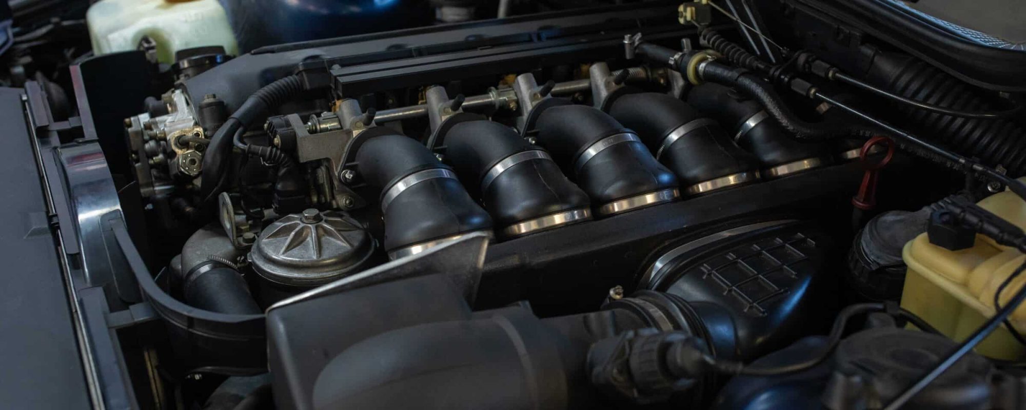 A detailed view of a BMW engine bay, highlighting the individual throttle bodies, intake manifold, and various engine components.